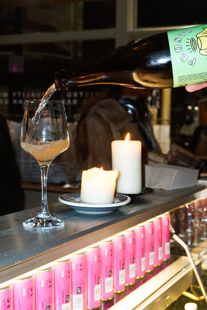 PROST! organic sparkling wine being poured into a glass at a candlelit bar with Loco Wines cans in the background