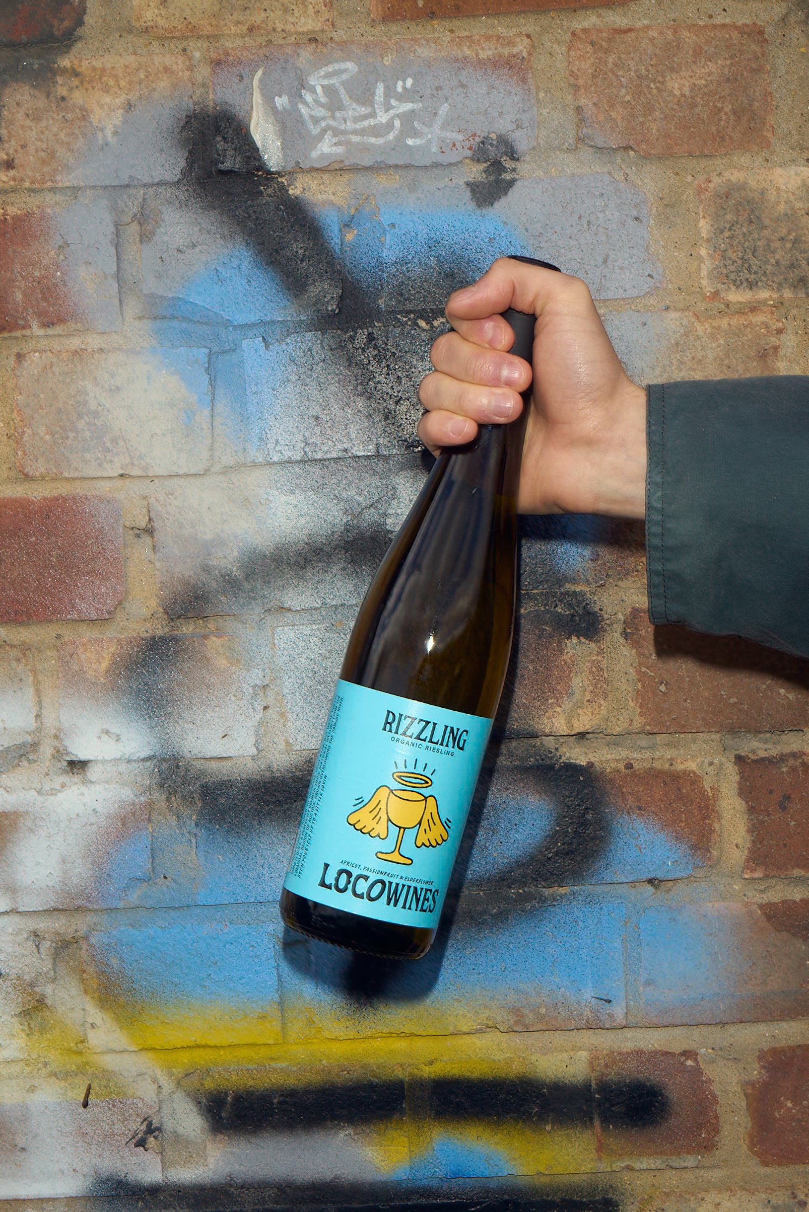 Rizzling organic Riesling white wine bottle held against graffiti brick wall by Loco Wines