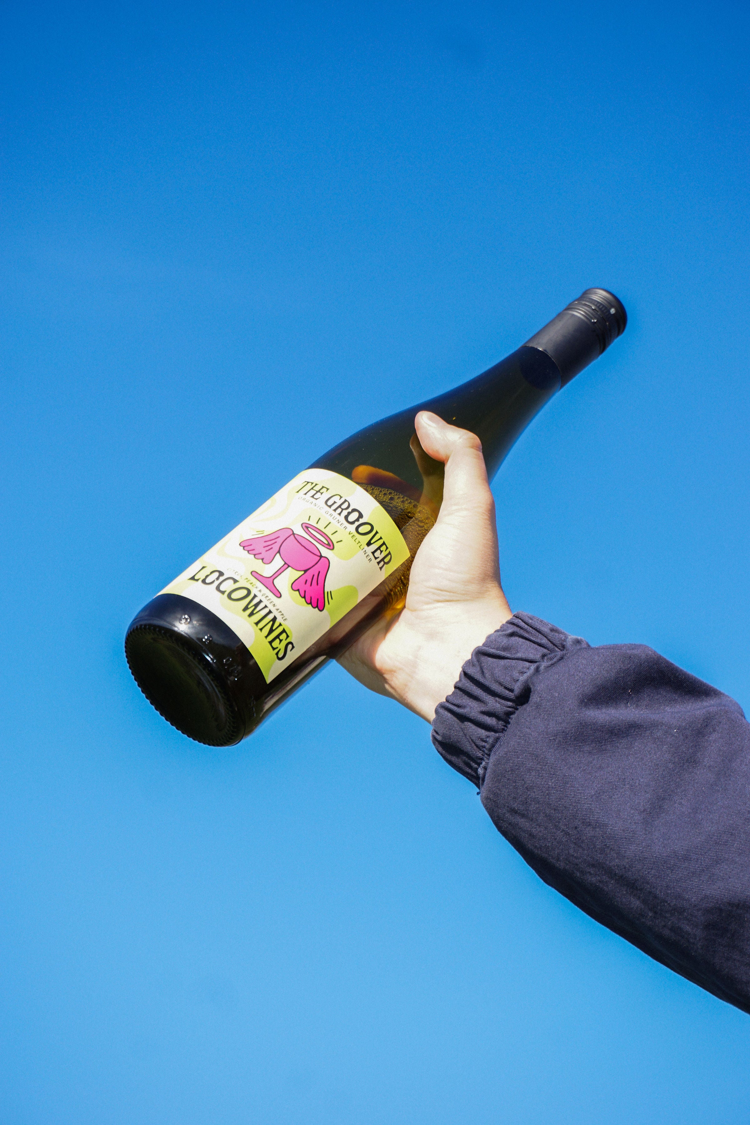 The Groover organic white wine bottle held up against a clear blue sky by Loco Wines
